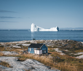 Typical wooden colourful blue fisher house with iceberg in Disko bay area Greenland and Ilulissat. Typical architecture in the arctic circle. Summer and blue sky. © Mathias
