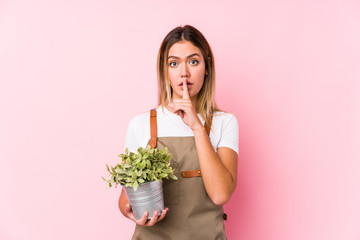 Young caucasian gardener woman in a pink background keeping a secret or asking for silence.