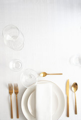 Table setting for elegant festive dinner with white porcelain plates, glasses, decorative textile and cutlery. Tableware background in white gold tone.