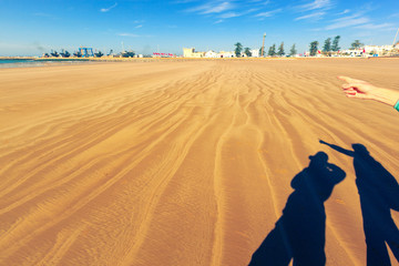 Fototapeta na wymiar Shadows on the golden sand - two people take picture of Essaouira port. Morocco