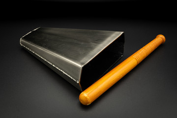 A bongo bell with stick lying on a black background
