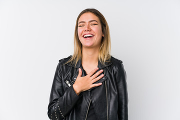Young caucasian woman wearing a black leather jacket laughs out loudly keeping hand on chest.