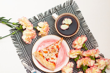 breakfast with cup of coffee, pizza and clove flowers on a checkered napkin