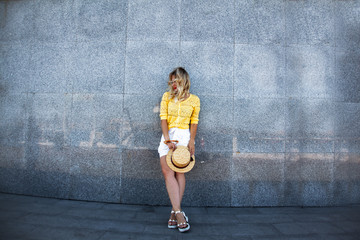 Pretty female model posing against the gray wall. Woman dressed urban style clothes , white shorts, yellow t-shirt and straw hat. The fashion street lifestyle of summer vacation.