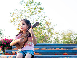 Little asian child girl play the ukulele, in the garden on the Steel pipe
