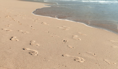 Footprints of bare feet are on wet sand of the beach
