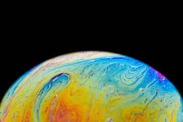 Rainbow soap bubble on an isolated black background. Close-up of the colorful surface. Poster blank