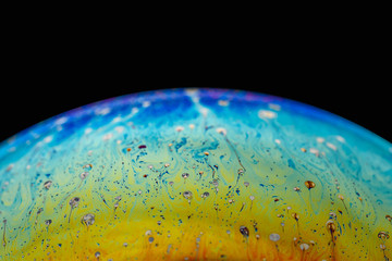 Rainbow soap bubble on an isolated black background. Close-up of the colorful surface. Poster blank