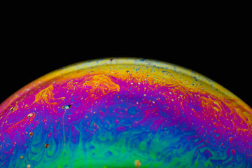 Rainbow soap bubble on an isolated black background. Close-up of the colorful surface. Poster blank