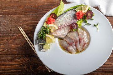 Light-salted dorado with sunflower in truffle oil. Next to slices of lemon, lime, grapes, pickled ginger. To the side of the plate are chopsticks.