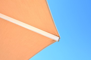 Part of beach folding umbrella on blue sky background. Summer background with sun parasol on blue sky backdrop. Summertime. Vacation concept. Vacation at the beach mock up. 