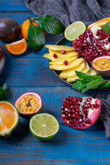 Pineapple slices, pomegranate, passion fruit and tangerines forming copy space on the blue wooden background