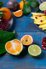 Pineapple slices, pomegranate, passion fruit and tangerines forming copy space on the blue wooden background