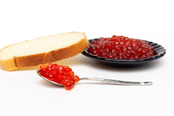 Red caviar on a spoon in the foreground and on a black plate with white bread