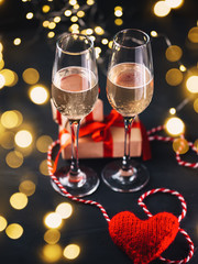 Glasses of champagne on a dark concrete table and a red heart with gifts. Celebrate Valentine's Day