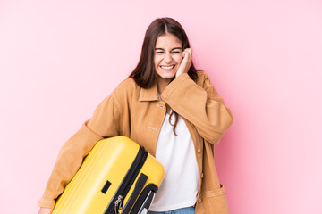 Young caucasian traveler woman holding a suitcase isolatedcovering ears with hands.