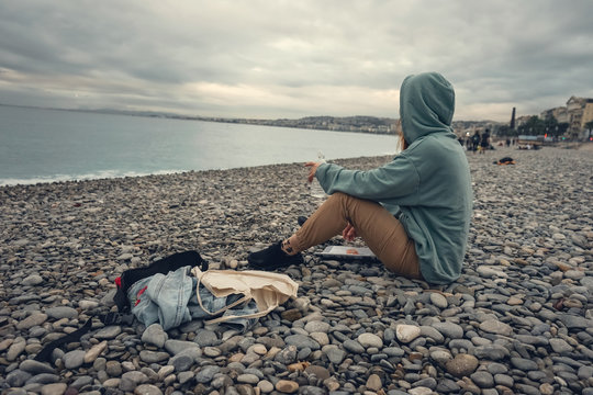 Woman Have A Rest Near Water On Nice Coast On Stones, Nice, France In Autumn. Evenong Near The Sea