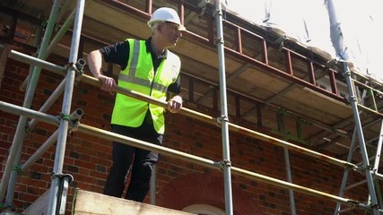 Male builder foreman, surveyor, worker or architect working on construction building site standing on scaffolding