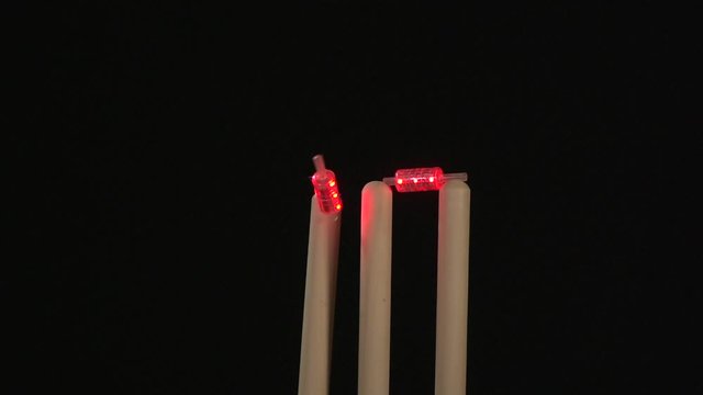Flashing Cricket Bails bowled out - The stumps are hit with the red ball. Black background. Super Slow motion