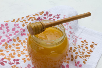Yellow honey in a glass jar with a wooden spoon on the background of a towel with flowers. sweet honey. beekeeper. natural sweets. honey is on the tablecloth. health food. space for text. menu.
