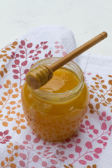 Yellow honey in a glass jar with a wooden spoon on the background of a towel with flowers. sweet honey. beekeeper. natural sweets. honey is on the tablecloth. health food. space for text. menu.