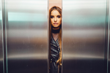 Elevator door from inside with blurred woman fashion model caucasian with black coat approaching between the opening or closing door metal metallic © Miljan Živković