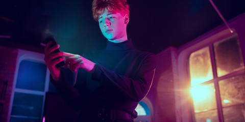 Calm, serious. Cinematic portrait of stylish redhair man in neon lighted interior. Toned like cinema effects in purple-blue. Caucasian model using smartphone in colorful lights indoors. Flyer.