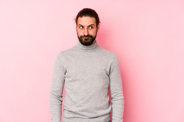 Young long hair man isolated on a pink background confused, feels doubtful and unsure.