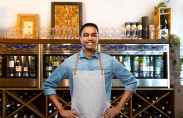 people, job and profession concept - smiling indian barman or waiter in apron over wine bar...