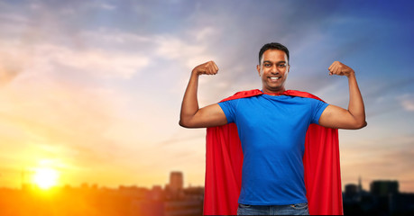 super power and people concept - indian man in red superhero cape showing his muscles over sunset...