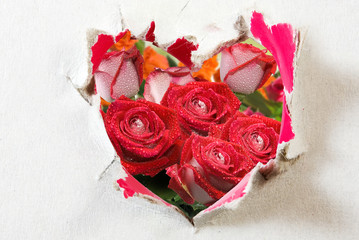 behind a sheet of paper is a bouquet of flowers in which a cut out in the form of a stylized heart is made