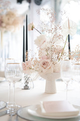 dinner table for dinner with plates, glasses and candles in a vase with roses, gypsophila and calla lilies in white and pink colors. Floral composition from a fresh bouquet for a wedding event.
