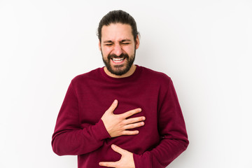 Young long hair man isolated on a white background laughs happily and has fun keeping hands on stomach.