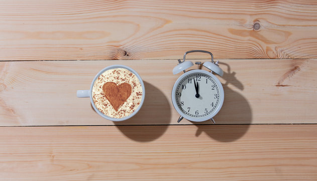Cup of coffee with heart shape and alarm clock on wooden table