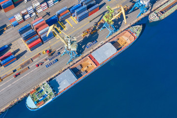 Aerial top view huge cargo ship moored at the pier at the port, loading goods, metal, concrete and other solid raw materials.