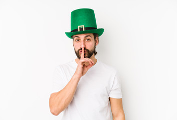 Young caucasian man wearing a saint patricks hat isolated keeping a secret or asking for silence.