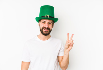 Young caucasian man wearing a saint patricks hat isolated joyful and carefree showing a peace symbol with fingers.