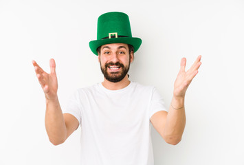 Young caucasian man wearing a saint patricks hat isolated receiving a pleasant surprise, excited...