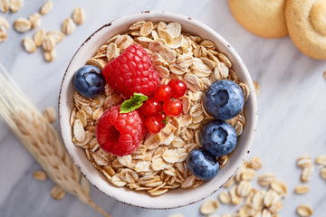 Oat meal healthy breakfast in a bowl with berrry fruits on a marble background. Top view