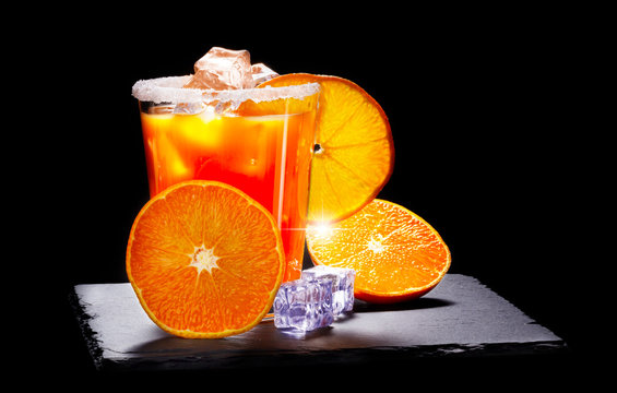 Orange juice with ice cubes, glass with a sugar rim on a slate board