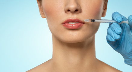 cosmetology, plastic surgery and beauty concept - beautiful young woman and hand with syringe making lifting injection over blue background