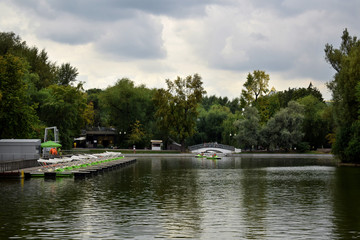 Fototapeta na wymiar Pond in the Gorky Park with boat rental station and a cafe in the background on a cloudy summer day