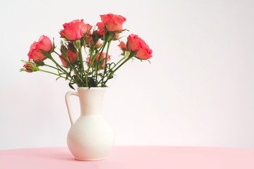 Bouquet of red roses in vase on a pink table on light background. Copy space