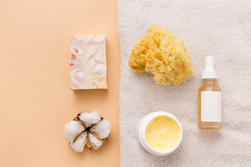 Fototapeta na wymiar beauty, spa and wellness concept - close up of crafted soap bar, body butter, natural sponge and essential oil on bath towel