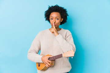 Young african american woman playing ukelele isolated keeping a secret or asking for silence.