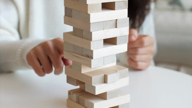 Close-up of young woman is pulling out the brick from wooden tower while family is playing board game together