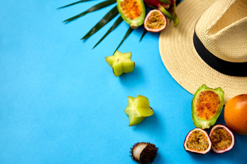 summer holidays, vacation and travel concept - close up of straw hat and exotic fruits on blue background
