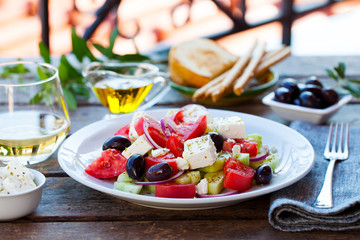 Greek salad. Fresh vegetables, feta cheese and black olives with white wine. Outdoor background.