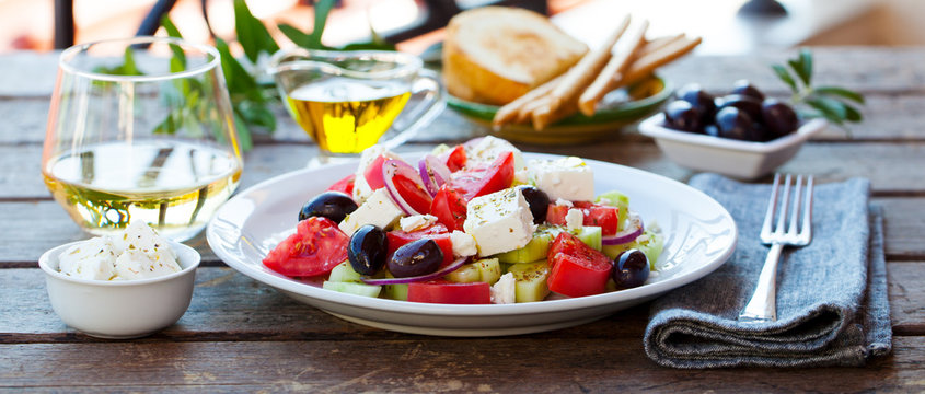 Greek salad. Fresh vegetables, feta cheese and black olives with white wine. Outdoor background.