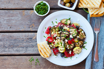 Grilled vegetables salad with feta cheese in white plate on wooden table. Copy space. Top view.